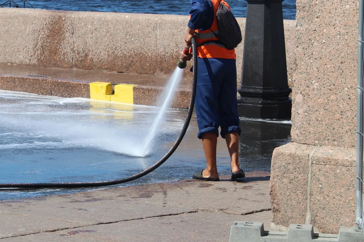 A worker in high-visibility gear pressure washing stone paving