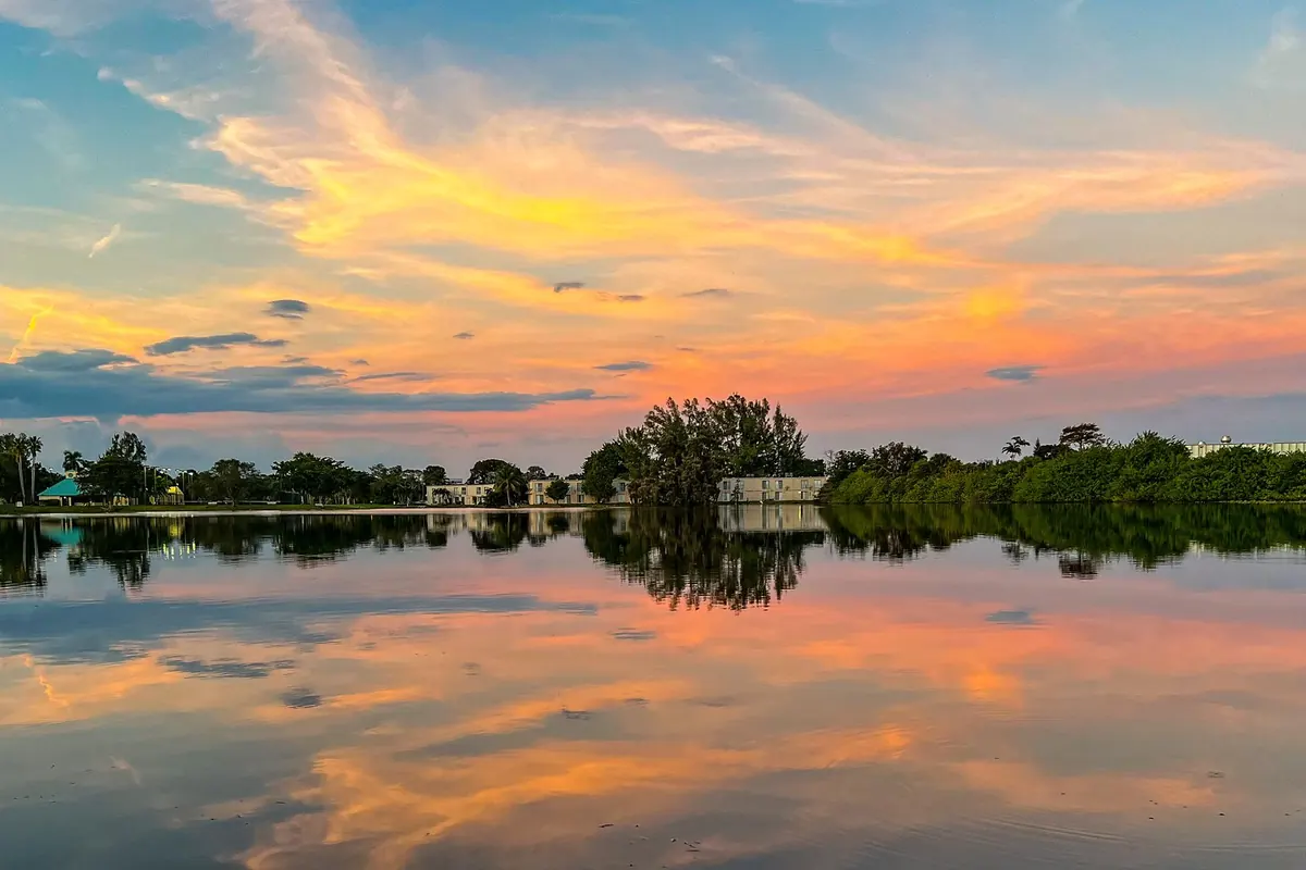 Homes and trees reflected in a still lake under a bright sunset