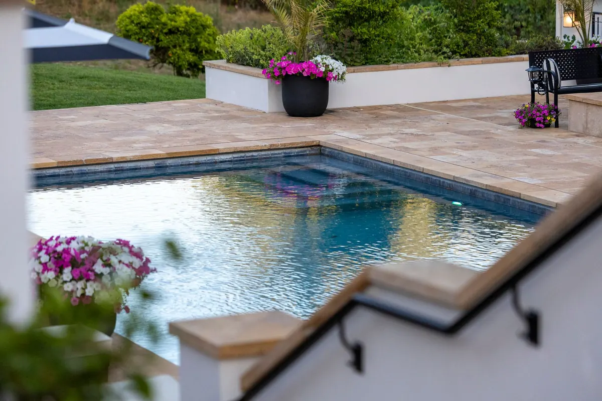 A clean paver pool deck around a small pool with flower planters