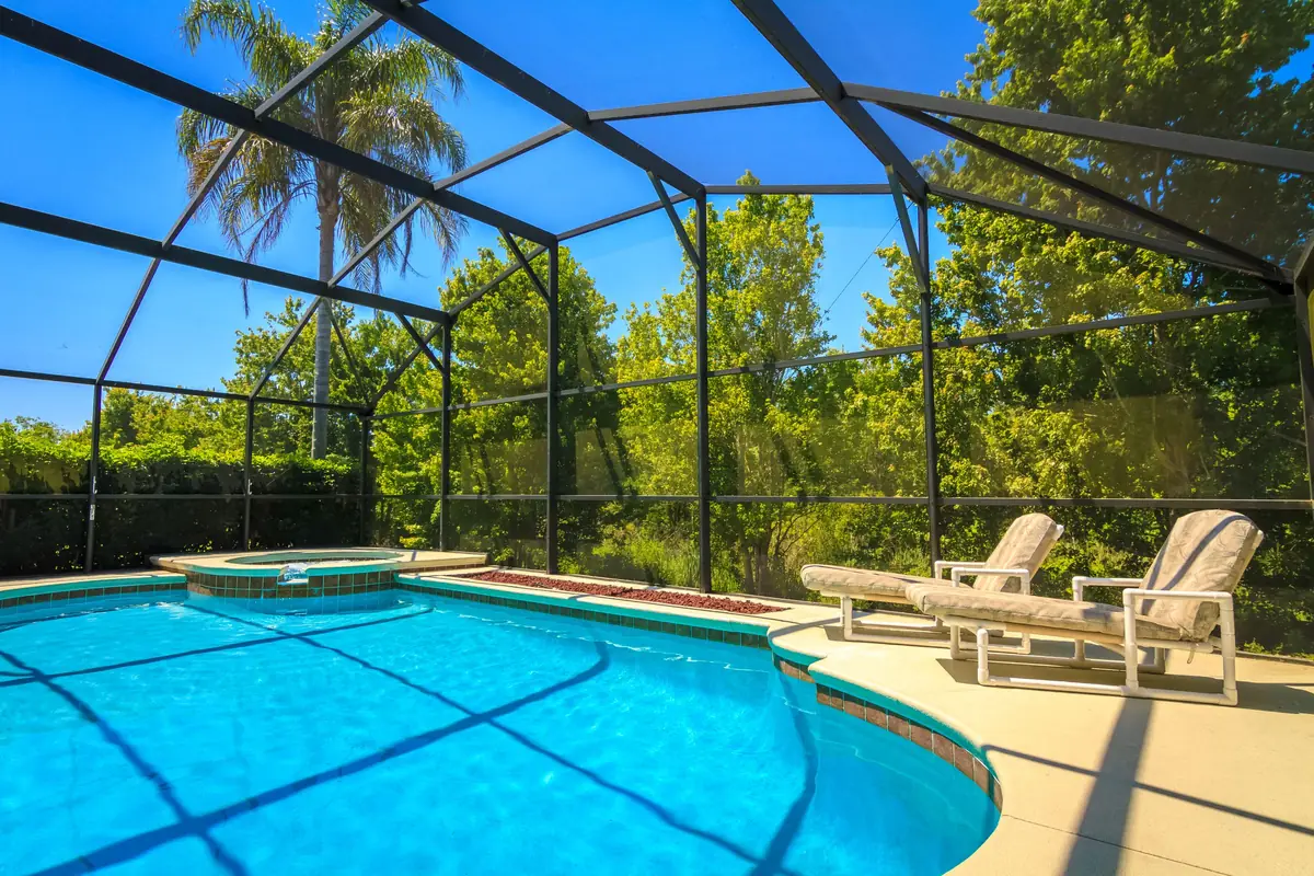 Screened aluminum pool enclosure over a backyard pool and spa with two loungers